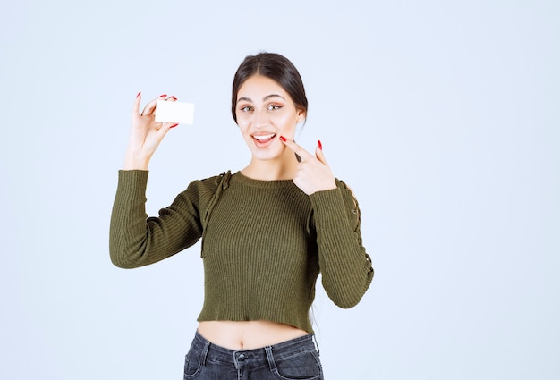 Free photo portrait of happy woman showing blank business card and pointing at her mouth.