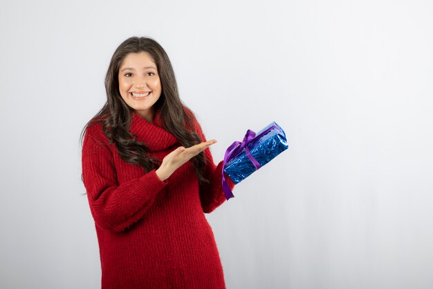 Portrait of a happy woman showing at a Christmas gift box with purple ribbon. 