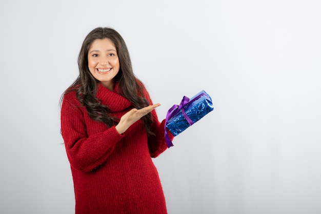 Portrait of a happy woman showing at a Christmas gift box with purple ribbon. 