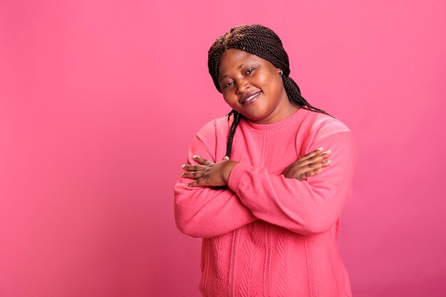 Portrait of happy woman smiling with confidence while posing in studio having cheerful expression enjoying shoot time. African american model with stylish hairstyle and pink sweather looking at camera