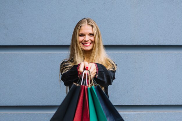 Portrait of a happy woman standing against wall holding shopping bags