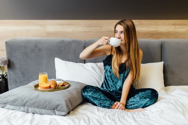 Портрет счастливой женщины, думающей и смотрящей на завтрак в отпуске в спальне