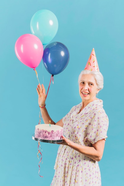 Ritratto di una donna felice con torta di compleanno e palloncini su sfondo blu