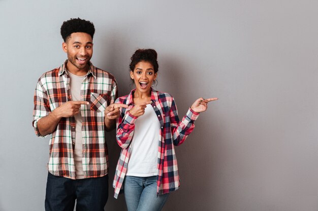 Portrait of a happy young african couple standing together pointing side with fingers