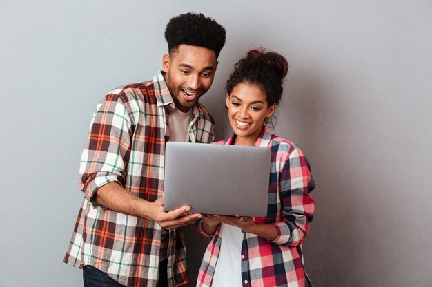 Портрет счастливой молодой африканской пары используя портативный компьютер