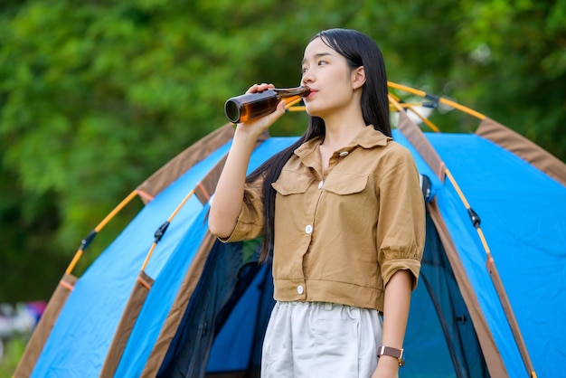 Portrait of happy young asian woman drinking a wate while standing in the camping site