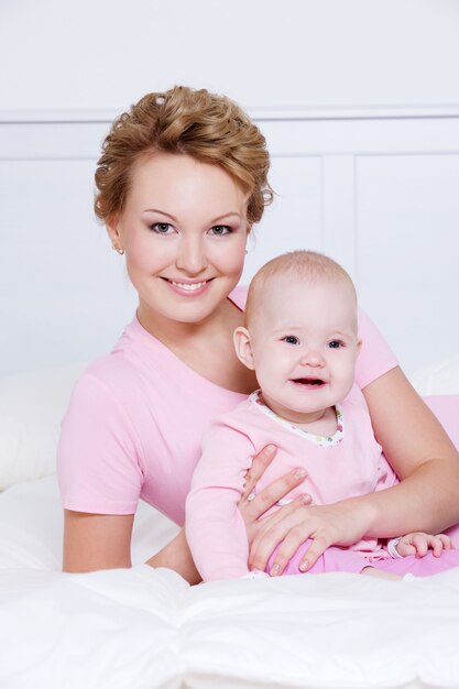 Portrait of happy young attactive mother lying with her baby on the bed at home