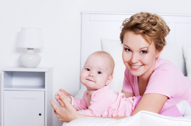 Portrait of happy young beautiful mother lying with her baby on the bed