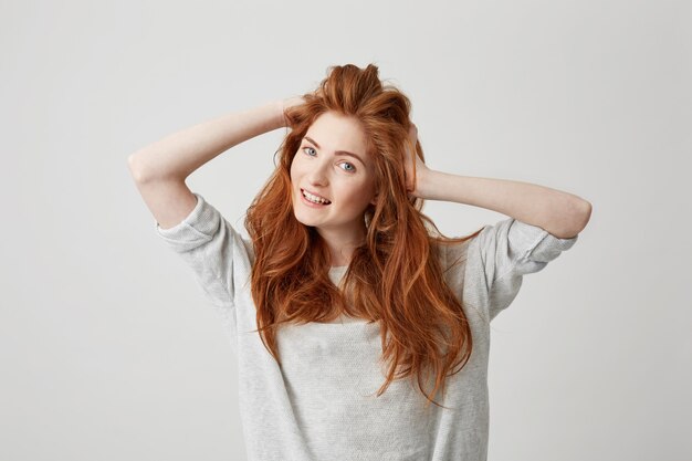 Portrait of happy young beautiful redhead girl smiling touching hair .