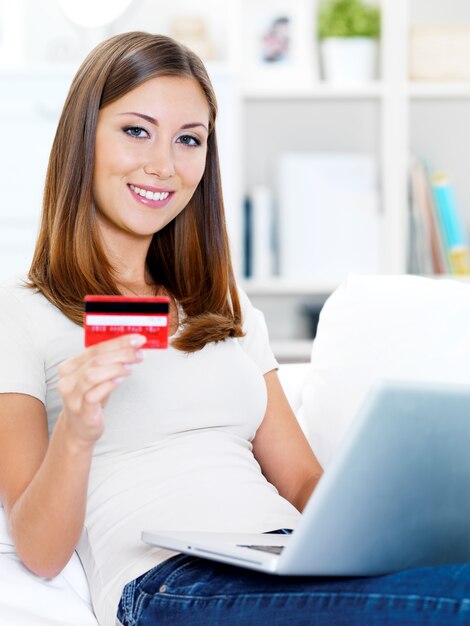 Portrait of happy young beautiful woman holding credit card and using laptop
