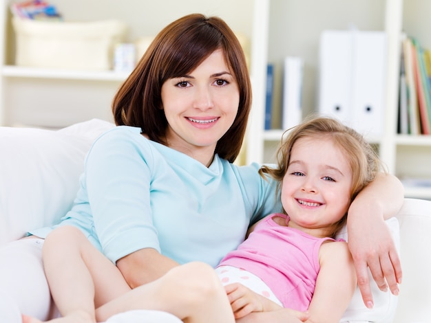 Portrait of happy young beautiful woman with little pretty daughter relaxing on a sofa at home