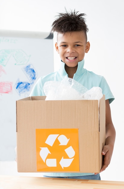 Free photo portrait of happy young boy holding recycling box