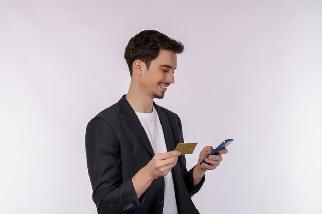 Portrait of happy young businessman standing using mobile cell phone and holding credit bank card isolated on white color background studio