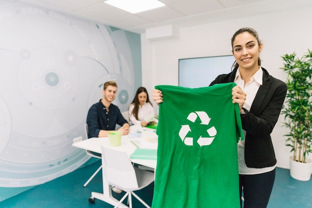 Foto gratuita ritratto di una giovane donna di affari felice che mostra maglietta verde con l'icona di riciclaggio