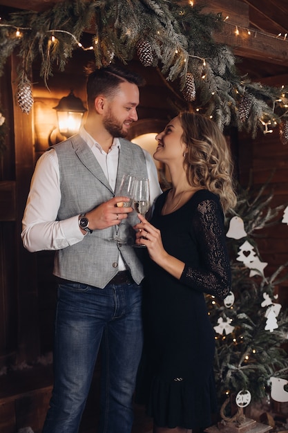 Портрет счастливой молодой пары в элегантных нарядах, улыбающейся лицом к лицу с двумя бокалами шампанского