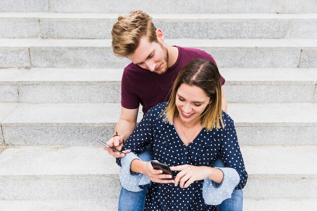 Portrait of a happy young couple sitting on staircase holding cellphone