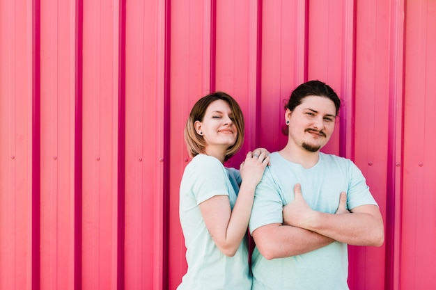 Portrait of happy young couple standing against pink corrugated metal sheet