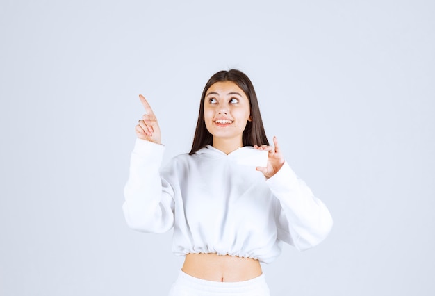 Portrait of a happy young girl model with a card pointing up.