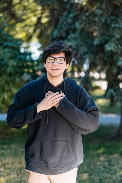 Portrait of happy young male student with glasses in casual outfit posing at the park.