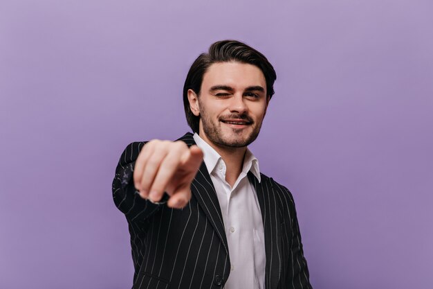 Portrait of happy young man dressed in white shirt, black suit looking straight while pointing to camera