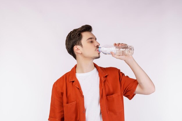 Portrait of Happy young man drinking water from a bottle and looking at camera isolated over white background