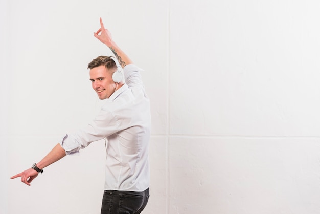 Free photo portrait of a happy young man listening music on headphone dancing against white wall