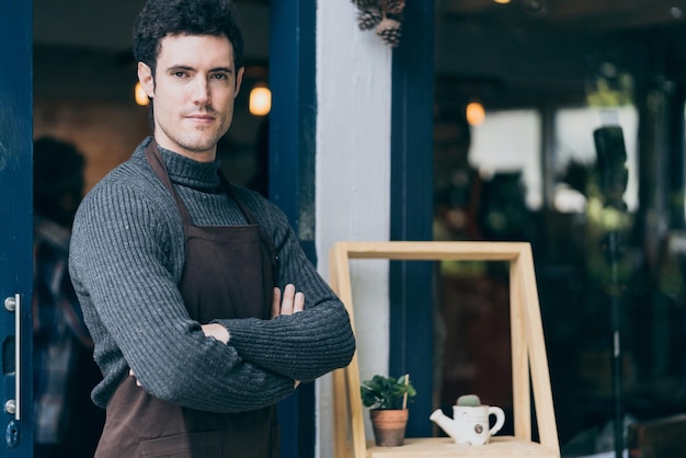 Free photo portrait of happy young man wearing an apron attractive caucasian male barista cafe restaurant owner cross arms and smile with confident and warm welcome to his successful business place