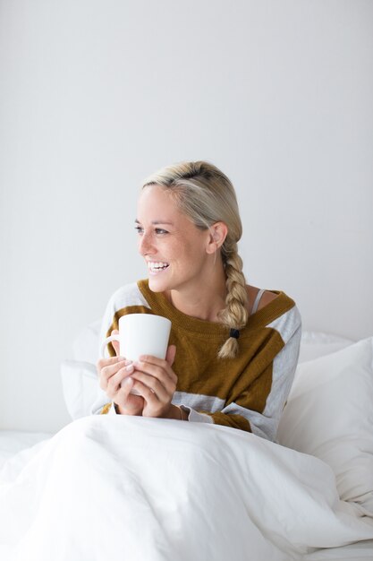 침대에서 차를 마시는 행복 한 젊은 여자의 초상화