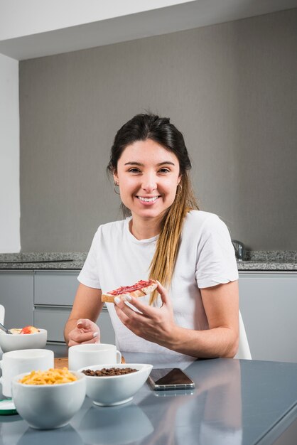 Portrait of a happy young woman holding bread with jam at breakfast table