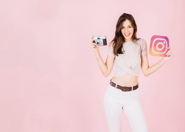 Portrait of a happy young woman holding camera and instagram icon