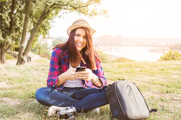 Ritratto di una giovane donna felice che tiene telefono cellulare nel parco