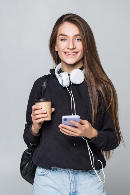 Portrait of happy young woman listening to music with mobile phone and earphones isolated on white wall