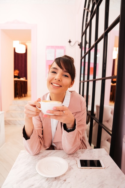 Ritratto di una giovane donna felice in giacca rosa bere caffè