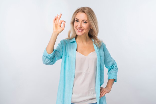 Portrait of a happy young woman showing ok sign against white backdrop
