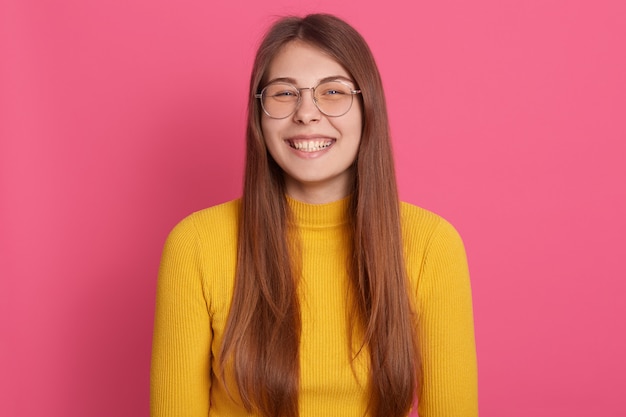 Portrait of happy young woman standing against pink wall. Caucasian female in casuals and glasses