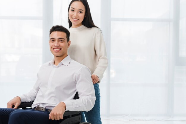 Portrait of a happy young woman standing behind the man sitting on wheelchair