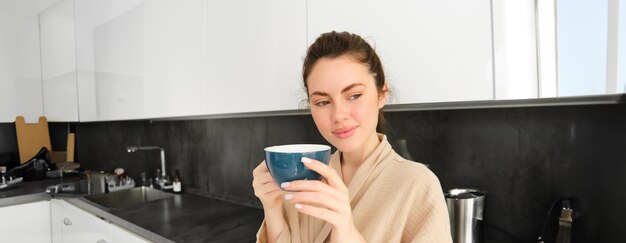 Free photo portrait of happy young woman starts her morning with mug of coffee drinking tea from cup standing