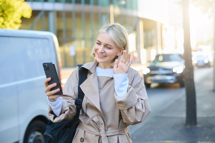 Free Photo portrait of happy young woman walking on street waving hello at smartphone camera connects to online