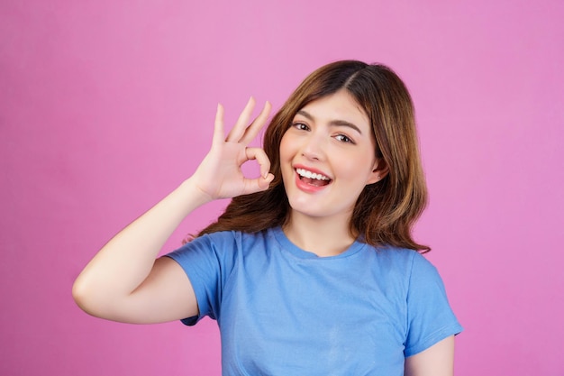 Портрет счастливой молодой женщины в повседневной футболке, показывающей рекламное решение oksign, хороший выбор на розовом фоне