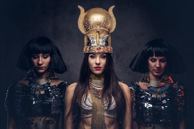 Портрет надменной египетской королевы в древнем костюме фараона с двумя наложницами. Изолированные на темном фоне.