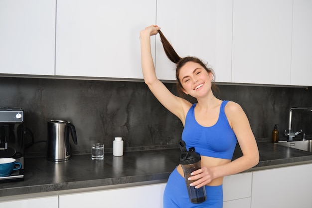 Free photo portrait of healthy beautiful brunette girl wearing fitness clothing standing in kitchen showing her