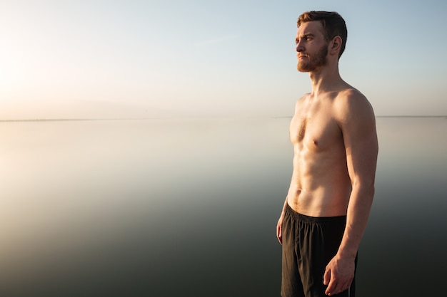 Foto gratuita ritratto di uno sportivo senza camicia sano in piedi all'aperto con acqua