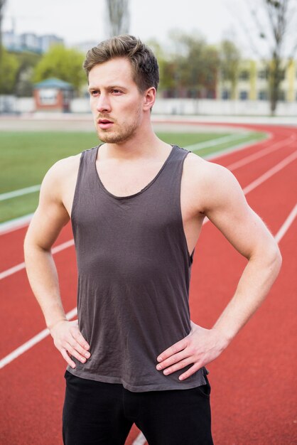 Portrait of healthy young man with hand on her hip standing on track field