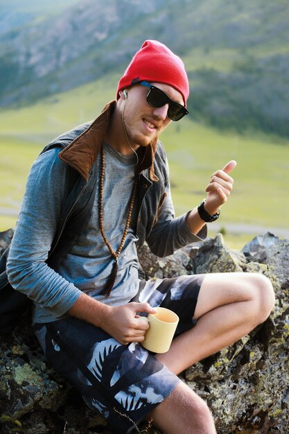 산을 여행하는 힙스터 남자의 초상화, 빨간 모자와 힙스터 옷을 입고, 사진을 찍습니다
