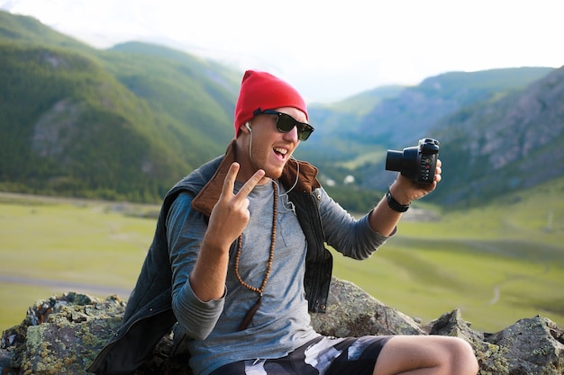 산을 여행하는 힙스터 남자의 초상화, 빨간 모자와 힙스터 옷을 입고, 사진을 찍습니다