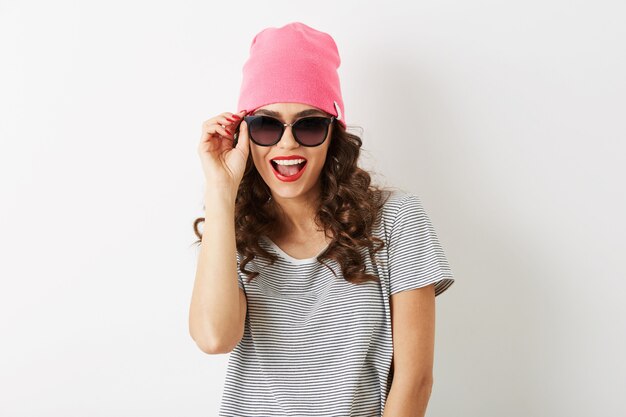 Portrait of hipster pretty woman with exited funny face expression, emotional, in pink hat, sunglasses, smiling, happy mood, isolated, white teeth, red lips, curly hair