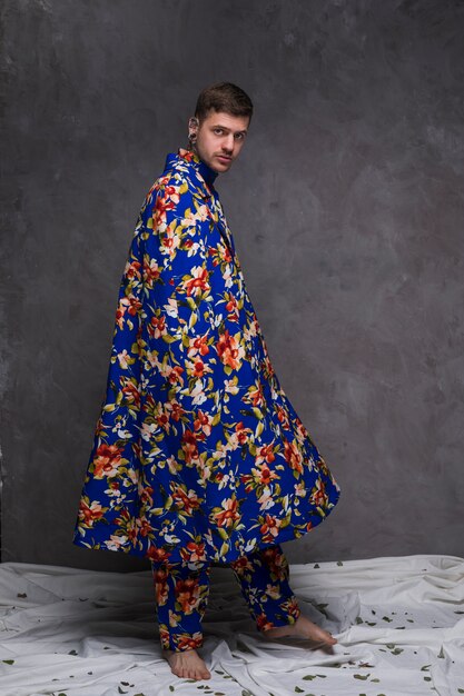 Portrait of a hipster young man with floral drape looking at camera against grey wall