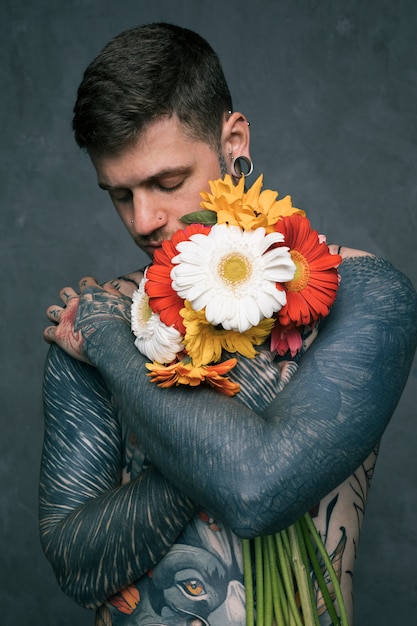 Foto gratuita ritratto di un giovane hipster con tatuato sul suo corpo che abbraccia i fiori di gerbera