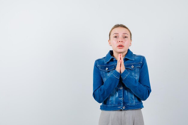 Portrait of hopeless attractive blonde in blue denim coat hands folded in praying position and begging for help isolated on white background