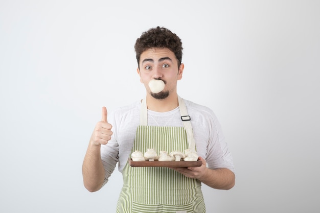 Portrait of hungry male cook holding raw mushrooms on white 